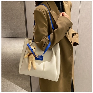 Dettaglio borsa tote in pelle crema con tracolla blu e ciondolo a forma di orsetto