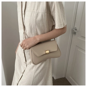 Detail of light beige curved shoulder bag with matte gold buckle on a linen dress