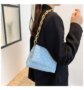 Close-up of light blue quilted shoulder bag with chunky gold chain strap and radial stitching