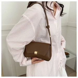 Close-up of brown baguette shoulder bag with gold buckle and unique knotted strap detail