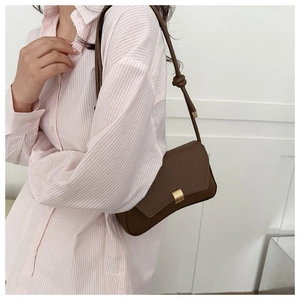 Detail of a minimalist brown leather square bag with a matte gold buckle on a model