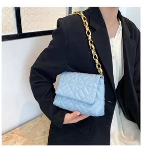 Detail of light blue quilted shoulder bag with chunky gold chain strap worn by model