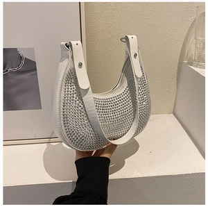 Detailed view of silver rhinestones on a white half-moon shoulder bag held by hand