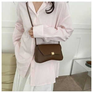Detail of a brown leather shoulder bag with a unique wavy base and gold rectangular clasp