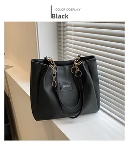 Detail of black leather tote bag with gold ring chain handles and fashion logo patch