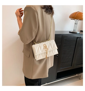 Detail of white quilted crossbody bag with golden chain strap and tassel on a model
