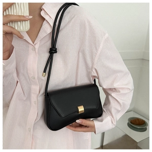 Detail of a minimalist black underarm bag with a golden metal buckle and decorative knot
