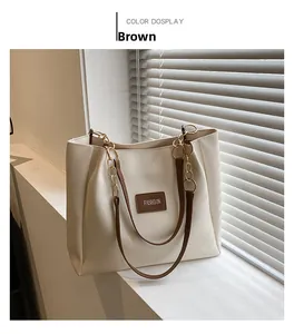 Detail of a large beige tote bag with brown straps and a stylish golden chain accent