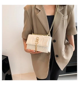 Detail view of a white quilted crossbody bag with gold S hardware and elegant chain strap