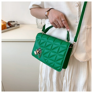 Detail of green quilted crossbody bag with golden lock held by a model in a cafe setting