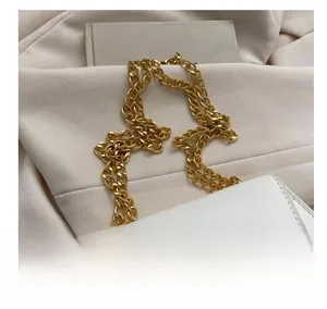Detail shot of a white crossbody bag featuring a chunky gold chain strap on a blazer
