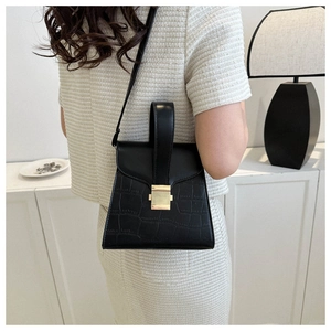 Détail du sac à main noir motif crocodile avec fermoir doré porté par le mannequin