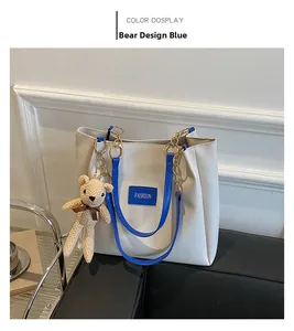 Detail of white tote bag with blue handles, fashion patch, and beige knit bear charm