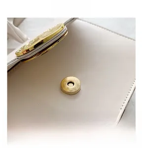 Détail du fermoir magnétique doré et des coutures fines sur le sac à main en cuir crème