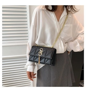 Detail of black quilted crossbody bag with gold S-logo, tassels and chain strap
