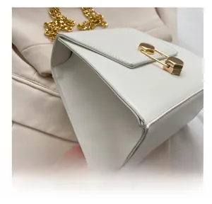 Detailed view of white trapezoid bag featuring gold pin lock and chain strap on fabric