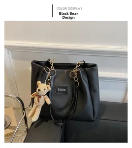 Detail of a black leather tote bag with gold chain handles and a brown bear charm