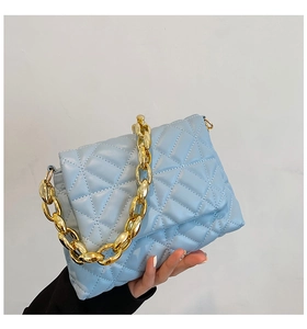 Close-up of sky blue quilted shoulder bag with chunky gold acrylic chain handle detail
