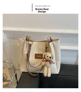 Detail of off-white faux leather tote bag with a beige knit bear charm and brown handles