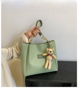 Detail of mint green tote bag featuring gold chain handles and a cute knit bear charm