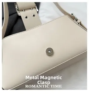 Detail of magnetic snap closure and wide strap with silver eyelets on cream shoulder bag