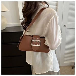 Detailed view of brown leather underarm bag with silver square buckle worn by a model
