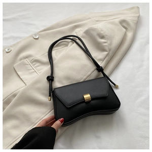Close-up of black crossbody bag with golden buckle and elegant knotted shoulder strap detail