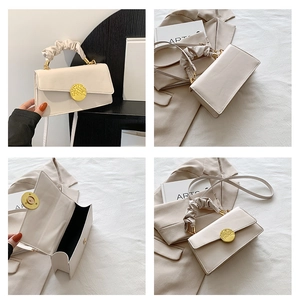 Detail of cream flap handbag with ruched handle and gold textured buckle closure