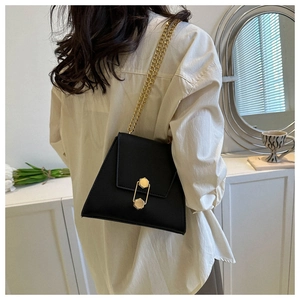 Detail of a black trapezoid bag with golden paperclip lock and fine metal chain strap