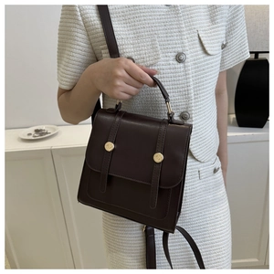 Detailed view of chocolate brown leather bag with golden buckles held by a model