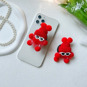 Red plush monster phone socket with sunglasses and knitted hat on a white phone case