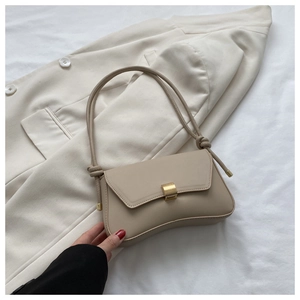 Close-up of beige leather baguette bag with metal buckle and knot strap detail