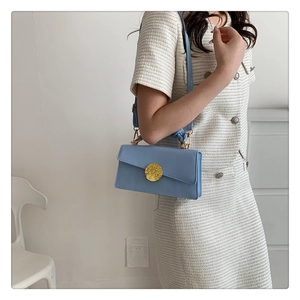 Détail du sac à bandoulière bleu ciel avec une grande boucle dorée à texture martelée