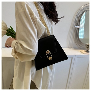 Detail of elegant black trapezoid bag with gold hexagonal clasp and delicate chain strap