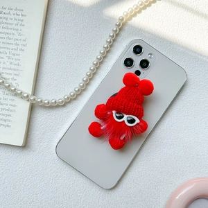 Detail of red plush monster phone grip with knit hat on a white smartphone