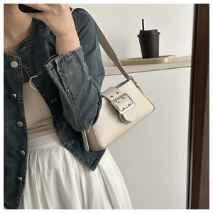 Close-up of cream shoulder bag featuring a large silver metal buckle and retro strap