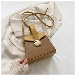 Détail du sac à main kaki motif crocodile avec fermoir doré sur une veste crème
