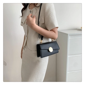 Détail d'un sac bandoulière noir minimaliste avec une boucle ronde dorée texturée