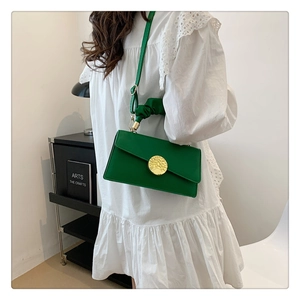 Detail of green leather crossbody bag featuring a large gold circular buckle and metal clasp