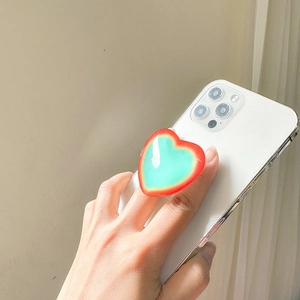 Close-up of heart-shaped phone grip with red and green gradient finish on white phone