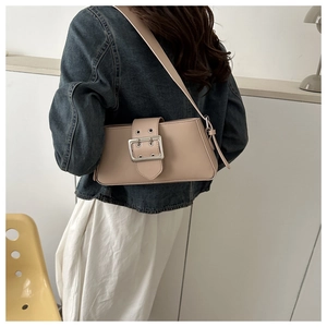 Detail of a minimalist beige underarm bag with a bold silver square buckle and leather strap