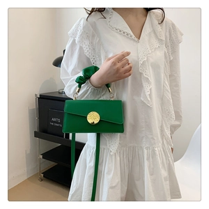 Détail du sac à main en cuir vert avec boucle dorée et poignée en tissu plissé