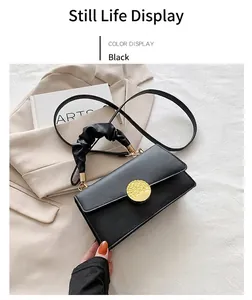Détail du sac à bandoulière noir avec boucle dorée et poignée froncée sur un blazer