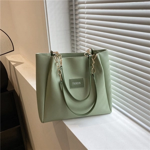 Elegante borsa tote verde salvia capiente con catena dorata in un interno minimalista