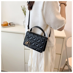 Detail of black quilted shoulder bag with golden lock and chain on a female model