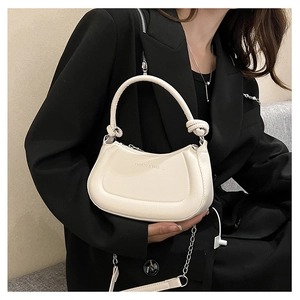 Detail of a creamy white crescent bag with knot decor and a fashion slogan text