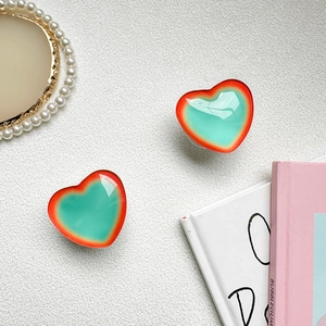 Detailed view of dual heart-shaped phone grips with gradient aurora finish on white desk