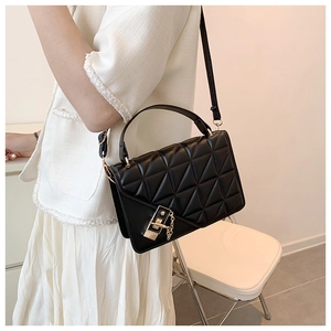 Detail of a black quilted leather handbag with gold metal lock and chain strap