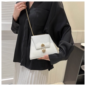 Close-up of white crossbody bag with gold safety pin buckle and chain strap on model