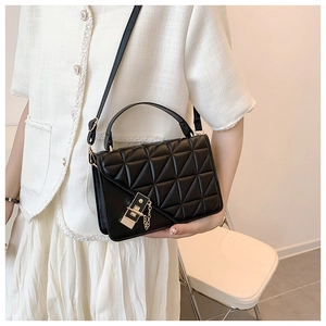 Close-up of black quilted leather crossbody bag with golden metal lock and chain detail